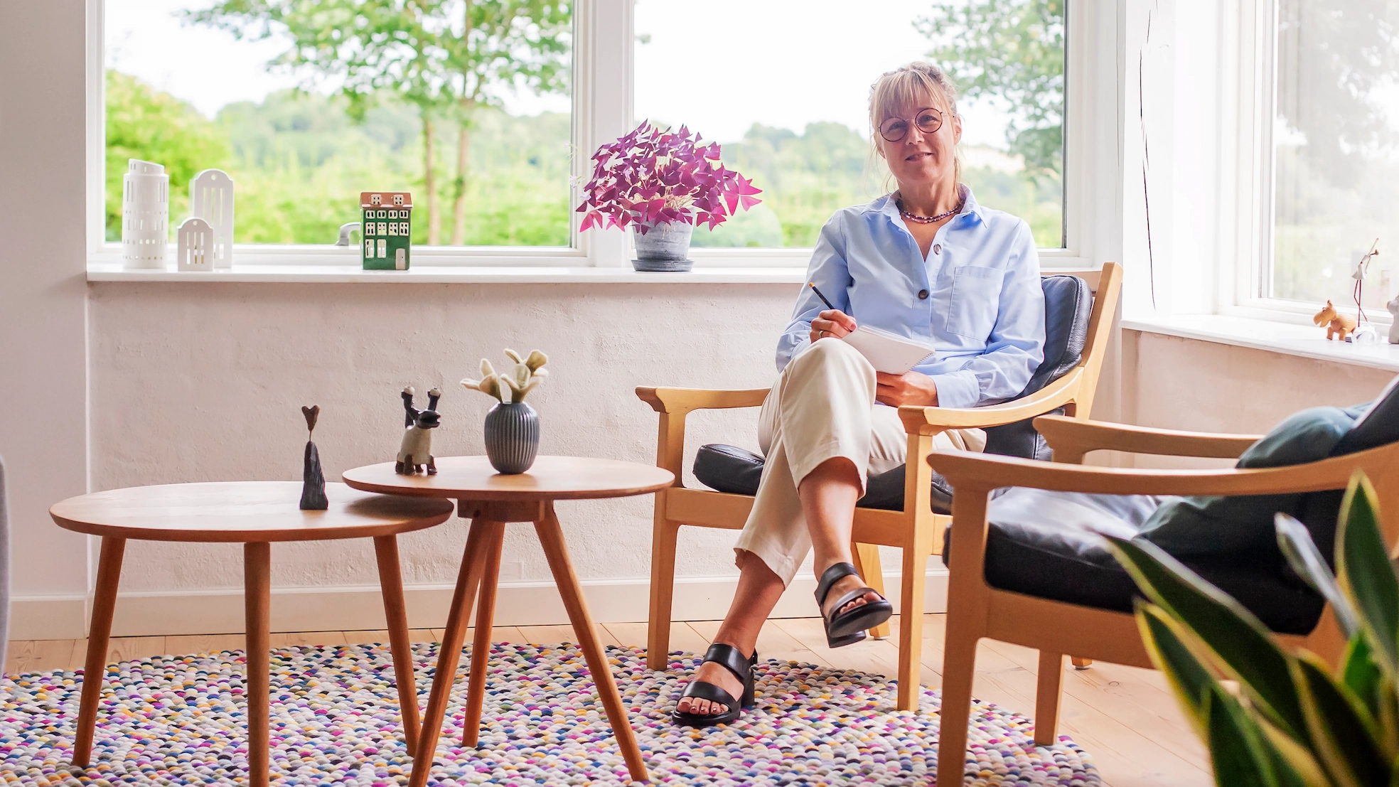 Therapist sitting in open room surrounded by green trees and plants outside